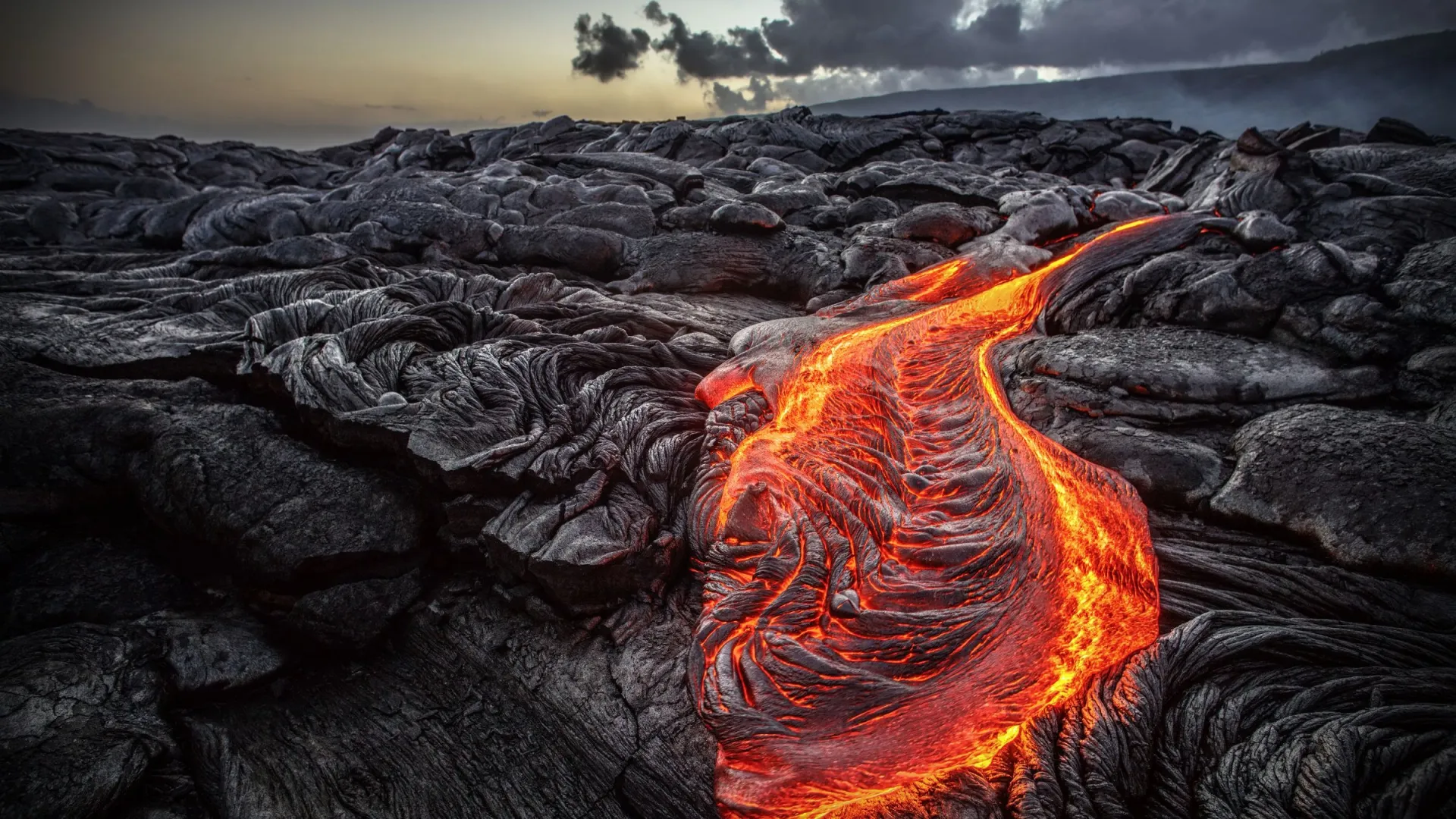 Flowing lava on dark volcanic rock at sunset.